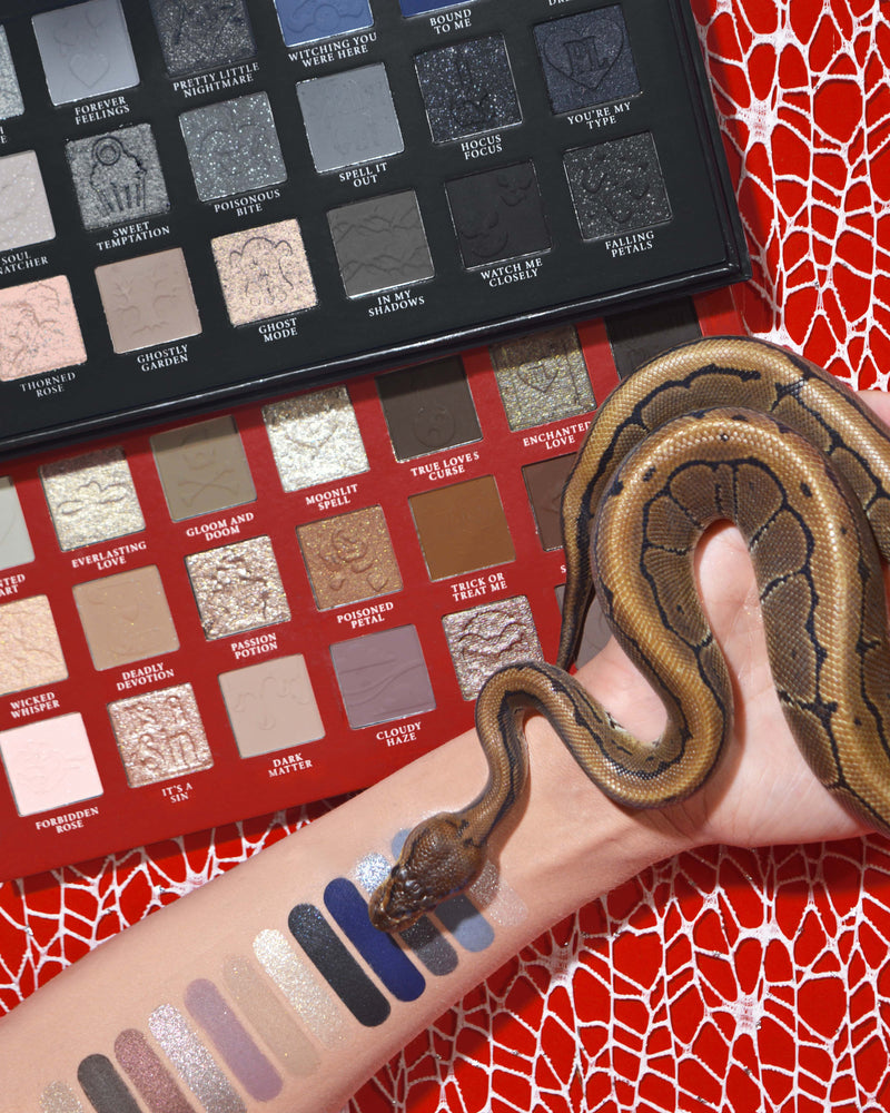 Paleta de sombras e maquiagem de Halloween P.Louise Mystic Moonlight com amostras em um braço com uma cobra enrolada em um fundo de teia de aranha vermelha