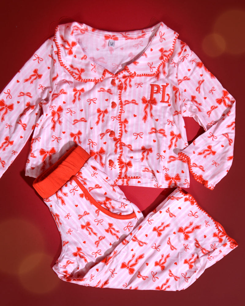 Conjunto de pijamas de Natal infantis listrados rosa e brancos com desenhos de laço vermelho sobre um fundo vermelho