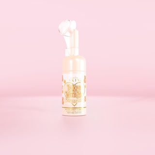 Una botella del limpiador facial espumoso P.Louise In Love With Me con aroma a pastel de coco sobre un fondo rosa