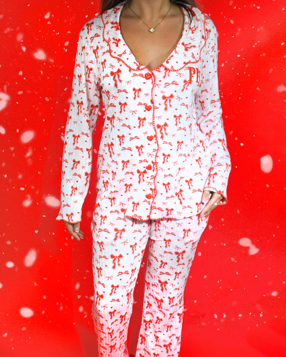 Foto do corpo de uma mulher vestindo um conjunto festivo de pijama listrado rosa e branco com desenhos de laço vermelho sobre um fundo vermelho e flocos de neve