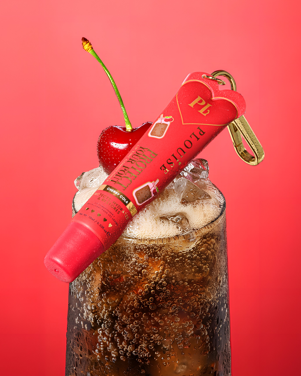 Tintura com aroma de cola de cereja vermelha protege seu beicinho condicionador de lábios com clipe dourado em cima de um copo de cola de cereja com uma cereja