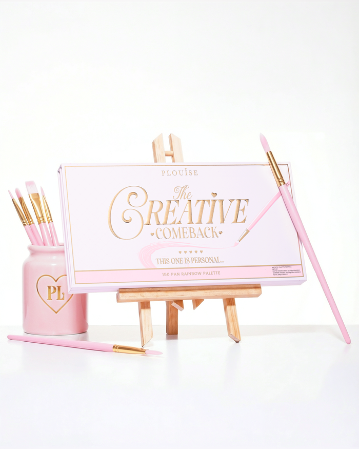 Uma paleta de sombras arco-íris P.Louise Creative Comeback XXXL rosa fechada colocada em um cavalete de arte cercado por pincéis de maquiagem