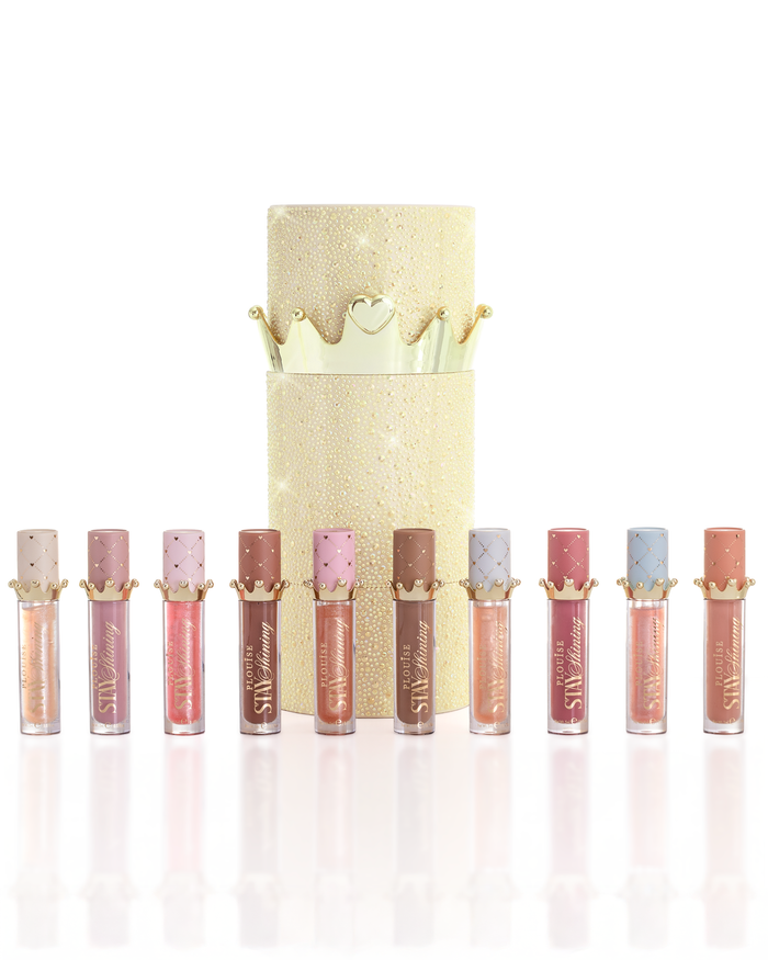 Un conjunto de diez productos de aceite para labios P.Louise Christmas Stay Shining dispuestos en fila frente a una caja de aceite para labios cilíndrica dorada brillante con una tapa de corona dorada, sobre un fondo blanco limpio.