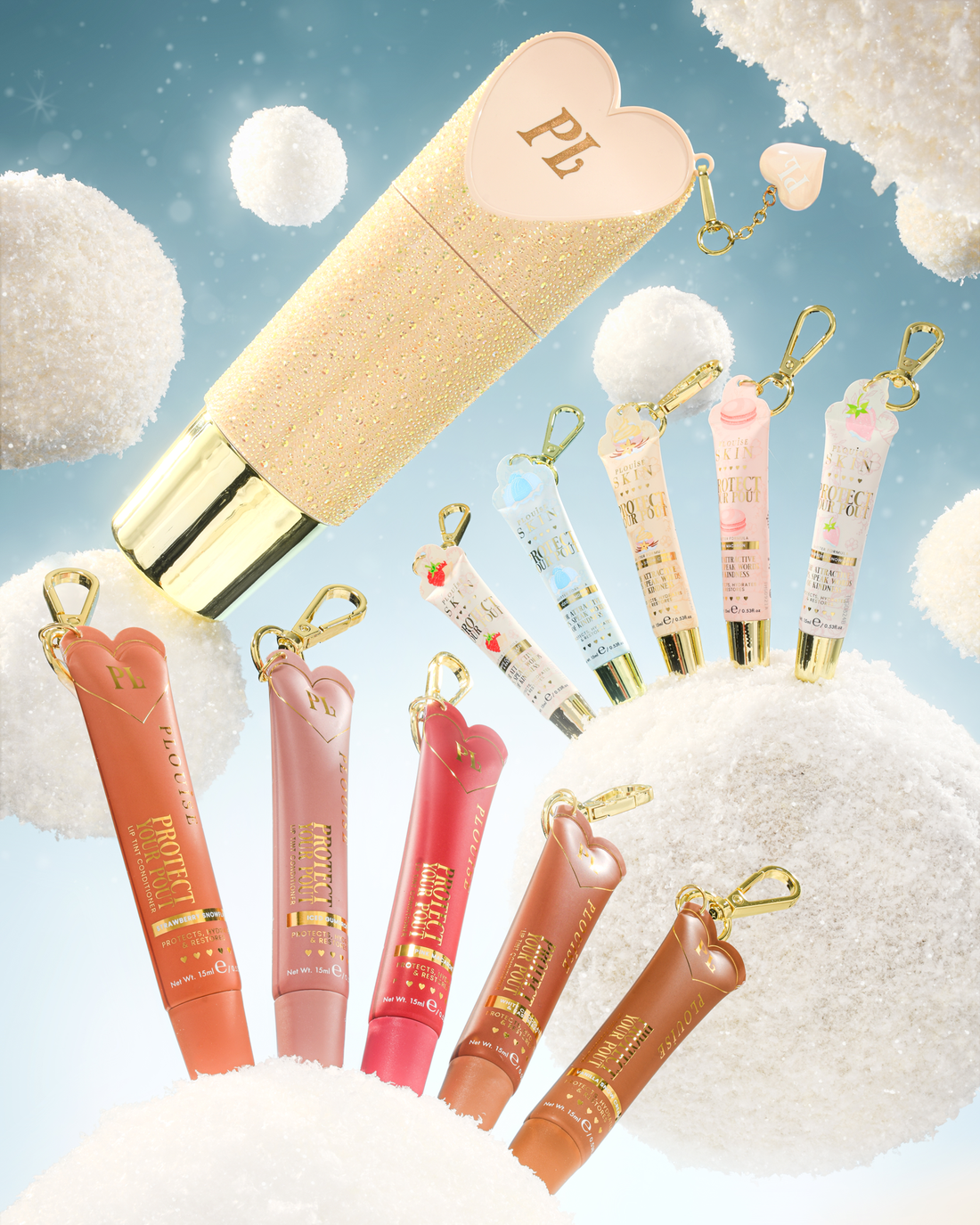 Um conjunto de tubos de chaveiro condicionador labial em forma de coração com chaveiros dourados, exibidos contra um fundo caprichoso de nuvens brancas fofas e um céu azul claro. O conjunto inclui um grande tubo de glitter dourado com uma tampa de coração rosa, vários tubos menores de brilho labial ou creme em tons de pêssego, rosa, vermelho e marrom e chaveiros menores em azul pastel e rosa.