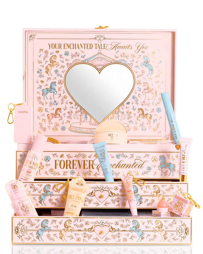 A P.Louise rosa pastel, azul e amarelo caixa de conjunto de presente de beleza de Natal PR rotulada 'Your Enchanted Tale' com um espelho em forma de coração na tampa e gavetas abertas, cercadas por diversos tubos de cosméticos, frascos e uma pequena bolsa em um fundo branco.
