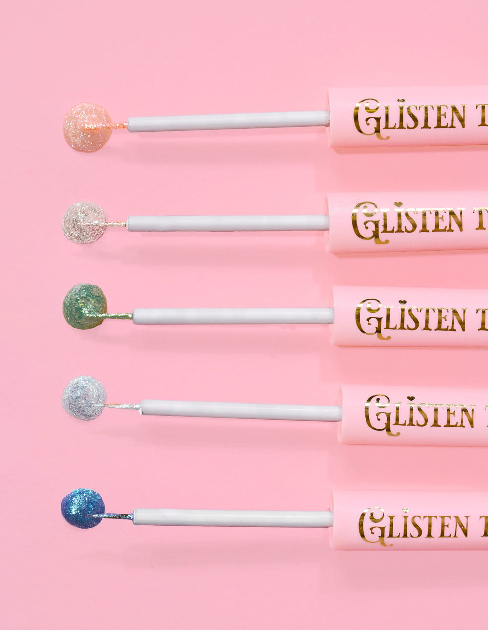 5 Delineadores com glitter P.Louise Glisten To Your Heart alinhados com uma gota do produto na ponta contra um fundo rosa
