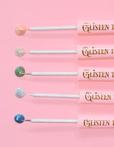 5 Delineadores com glitter P.Louise Glisten To Your Heart alinhados com uma gota do produto na ponta contra um fundo rosa