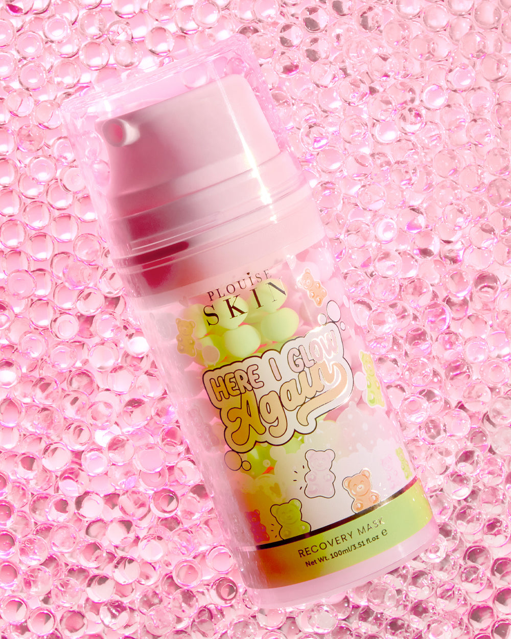 Um frasco de máscara de recuperação P.Louise Here I Glow Again com aroma de ursinhos doces com rótulo rosa e verde, com ilustrações de ursinhos doces, colocados sobre um fundo rosa brilhante.
