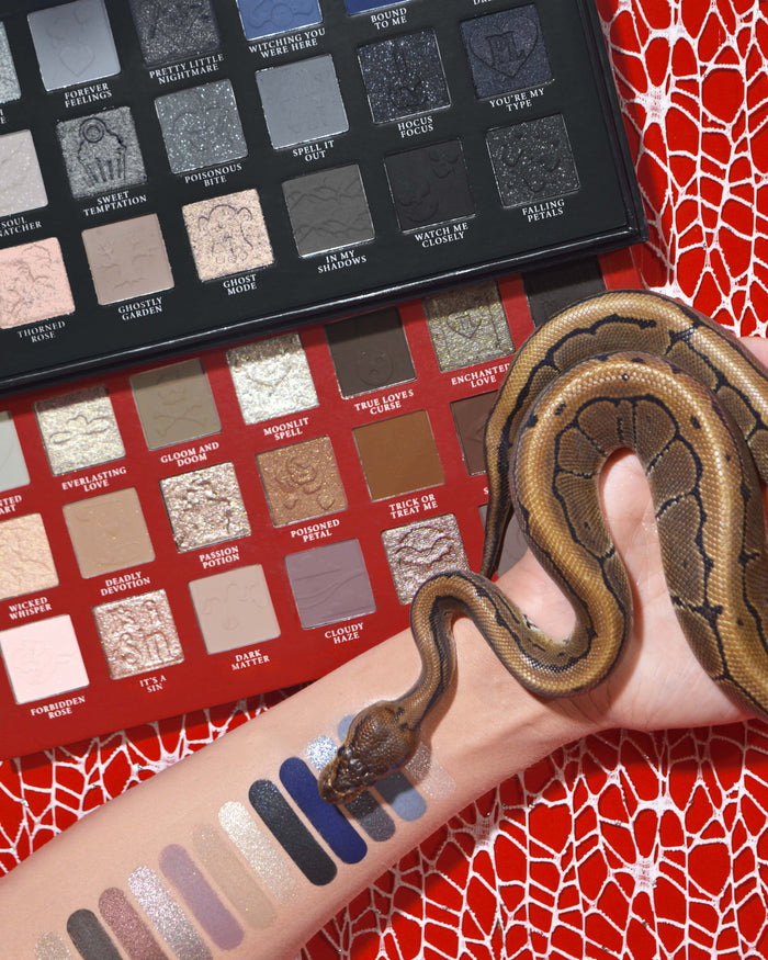 Paleta de sombras de ojos y maquillaje de Halloween P.Louise Mystic Moonlight con muestras en un brazo con una serpiente envuelta alrededor sobre un fondo de telaraña roja