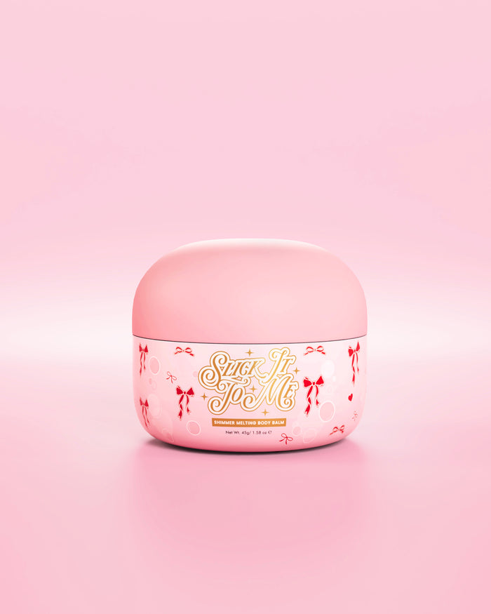 Tina rosa de bálsamo corporal derretido brillante SLick It To Me con elementos decorativos de lazo rojo sobre un fondo rosa