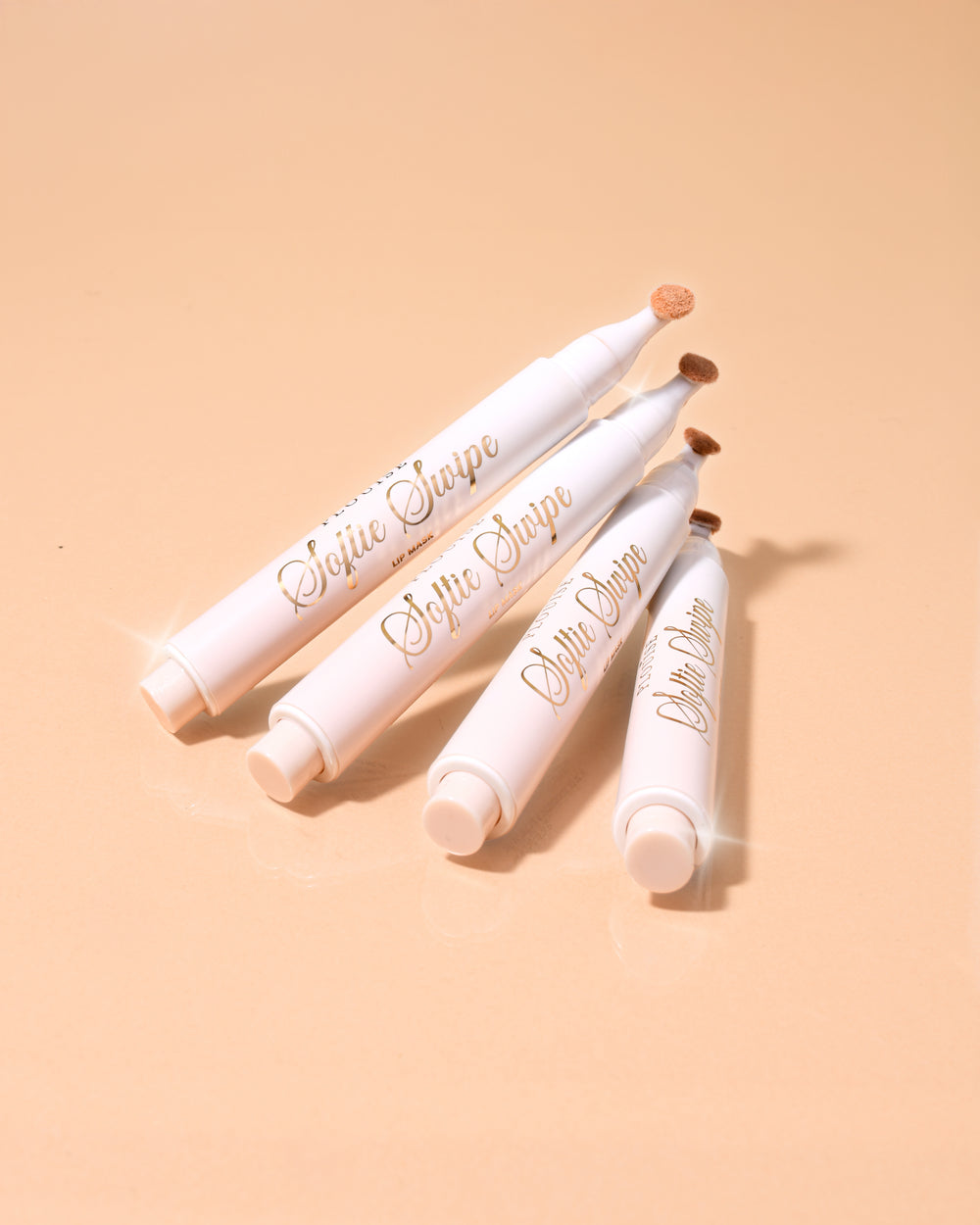 Una imagen de cuatro mascarillas de labios con color P.Louise Softie Swipe con aroma a pastel de coco apiladas una contra otra con un fondo beige