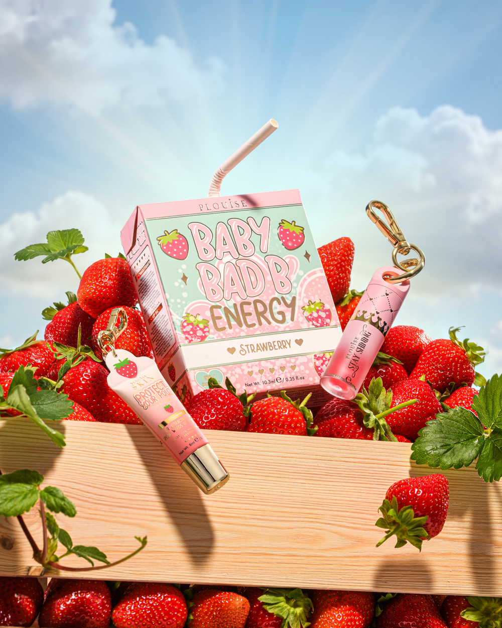 P.Louise Strawberry Baby Bad B Mini Lip Oil y Mini Lip Conditioner sobre una mesa rodeada de fresas