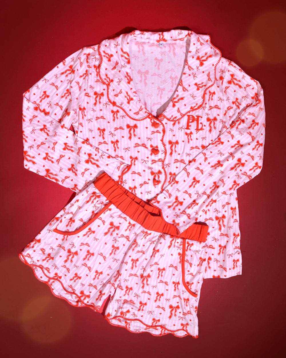 Imagem de pijamas adultos de Natal listrados rosa e branco com desenhos de laço vermelho em um fundo vermelho