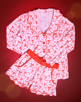 Imagem de pijamas adultos de Natal listrados rosa e branco com desenhos de laço vermelho em um fundo vermelho