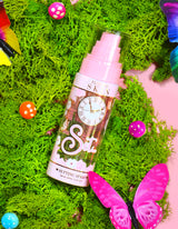 Um frasco de spray de configuração de longa duração P. Louise Ready Set Slay cercado por elementos decorativos, incluindo musgo falso colorido, borboletas e cogumelos.