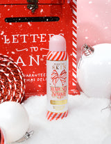 Una botella de spray fijador de purpurina navideña P. Louise Ready Set Sparkle rodeada de adornos festivos como nieve, adornos y un buzón navideño.
