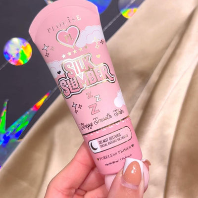 Uma pessoa segurando um tubo de P.Louise Silk Slumber Poreless Primer com fundo rosa e detalhes de produtos cosméticos.