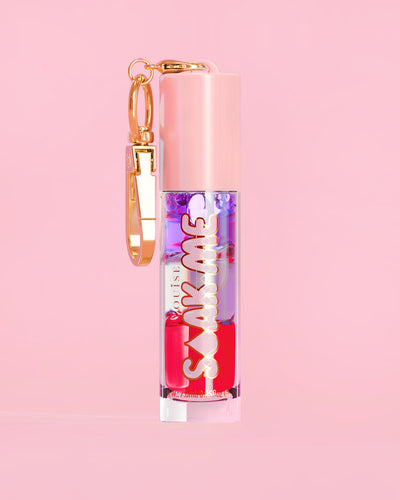 P. Louise Soak Me Lip Oil con aceite en capas de colores en un tubo rosa con un cierre dorado sobre un fondo rosa