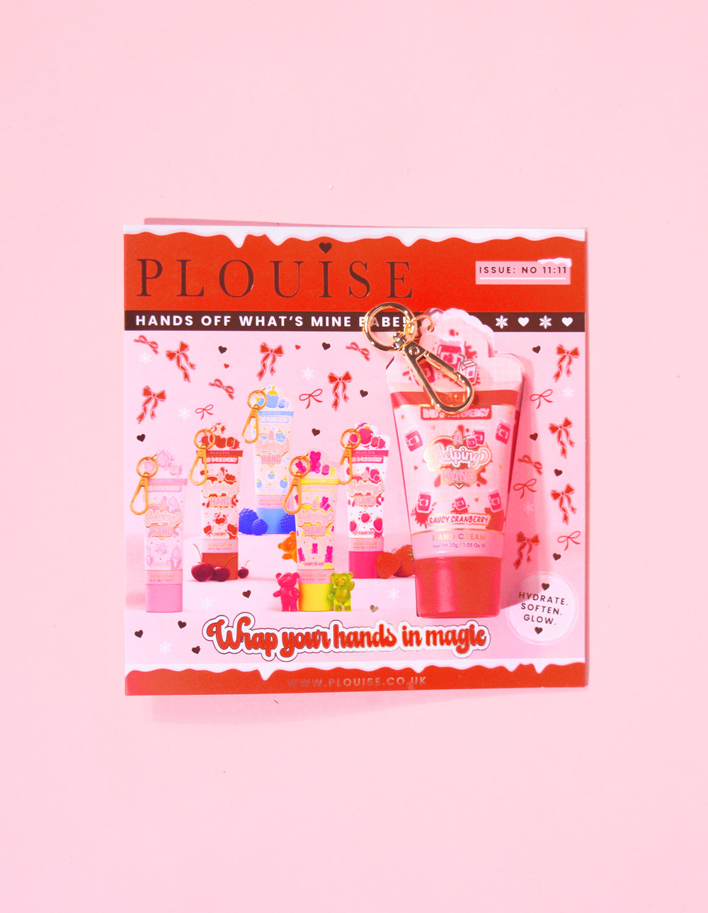 Revista de Natal P.Louise com um mini chaveiro com creme para as mãos picante de cranberry anexado à revista com um design festivo vermelho e rosa