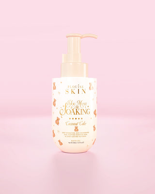Garrafa de P.Louise You Must Be Mergulhando óleo de banho em bolo de coco contra fundo rosa