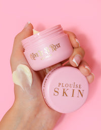 Una persona sosteniendo un frasco rosa de crema para ojos P.Louise Give It A Rest sin la tapa, mostrando el nombre del producto y la marca en el frasco.
