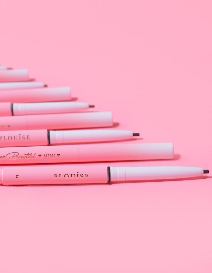 Uma coleção de Mini Lápis de Sobrancelha P.Louise dispostos em uma fileira com o nome da marca visível no corpo dos lápis, exibidos contra um fundo rosa